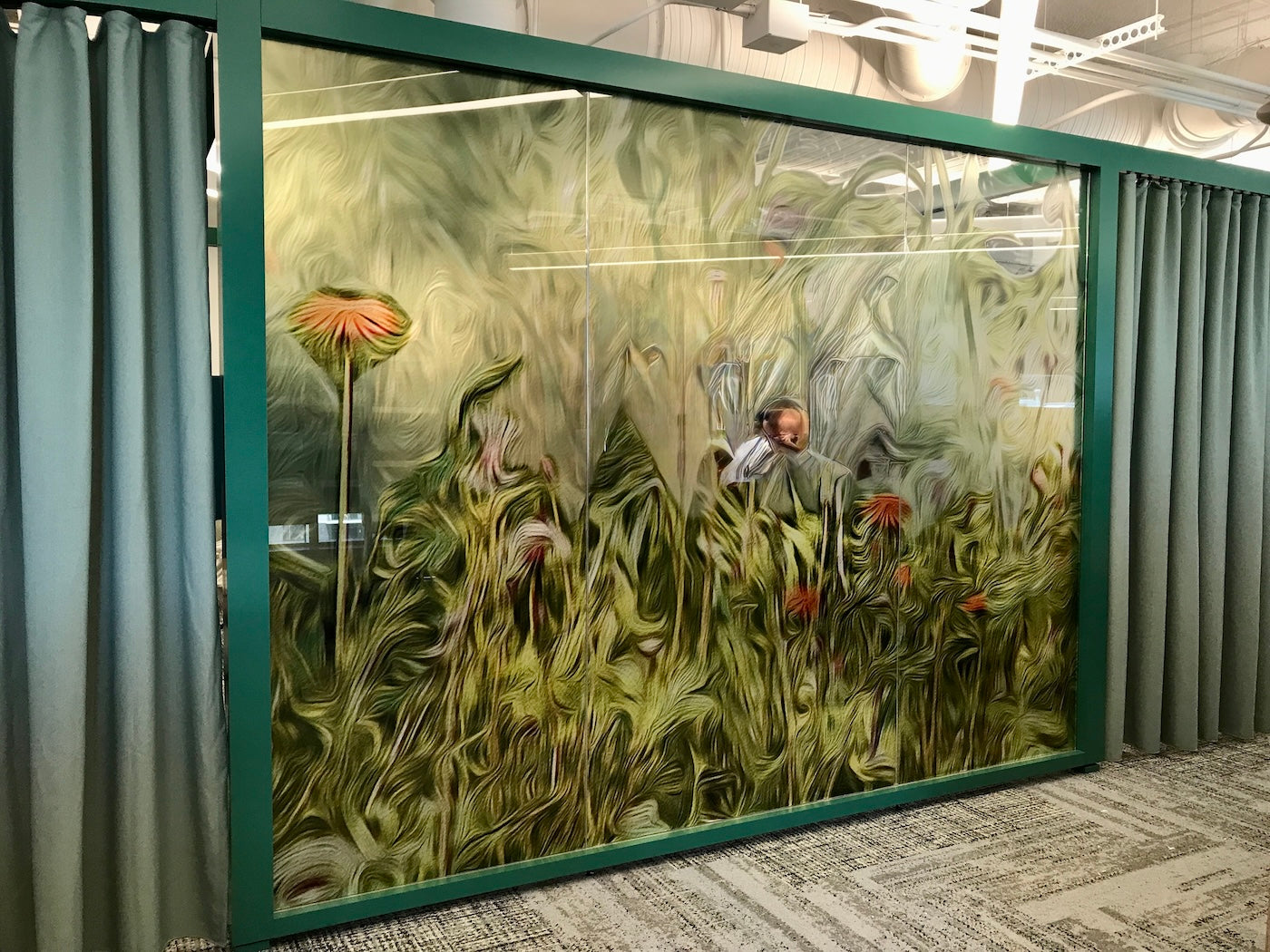 Banner: Large glass panel framed in teal featuring Pedernales Spring Yellow by Nancy Wood, an abstract botanical design in swirling greens and yellows with pops of pink-orange. The textured pattern fully obscures the view into the room, resembling tall, blurred wildflowers.