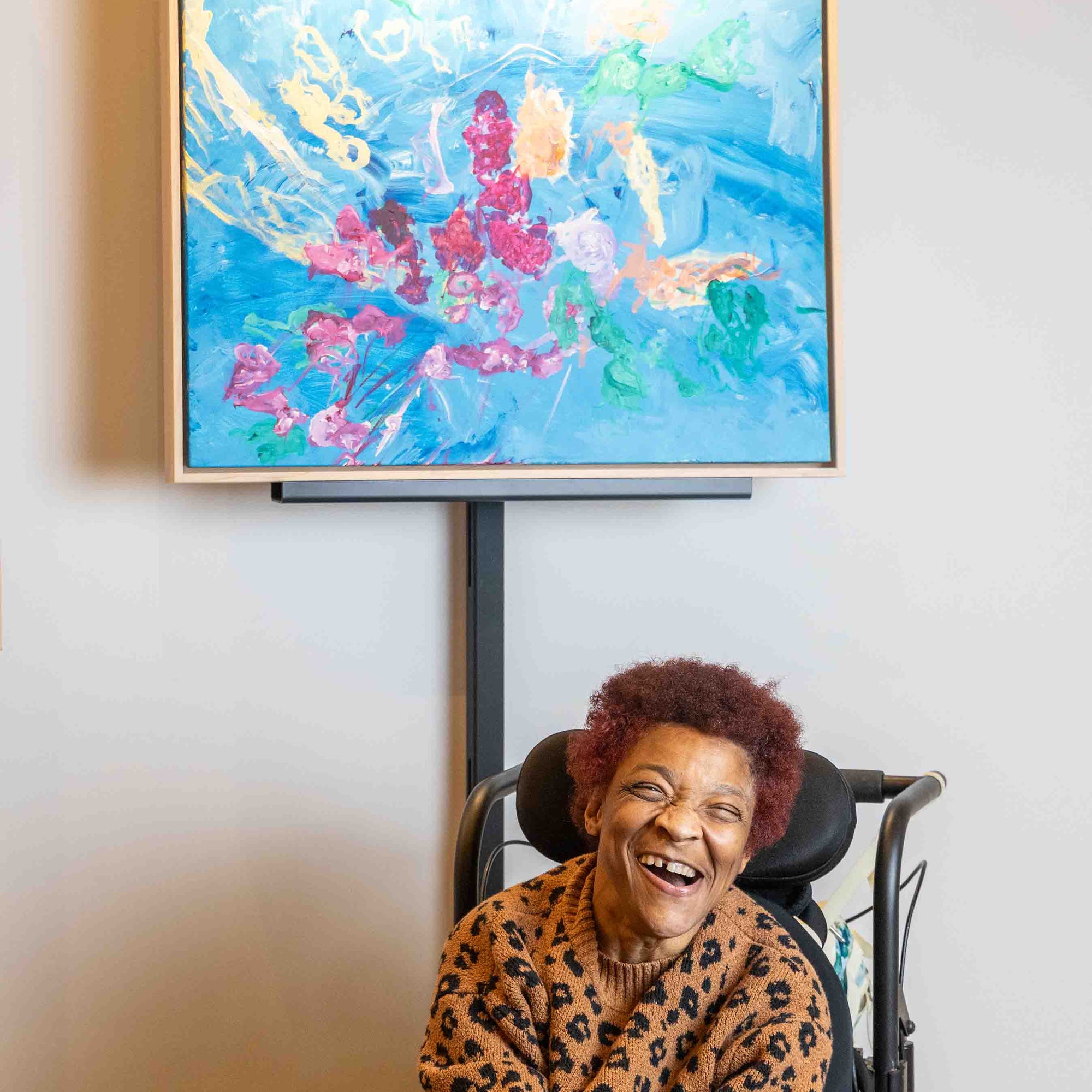 Person smiling in front of a colorful abstract painting on a wall.