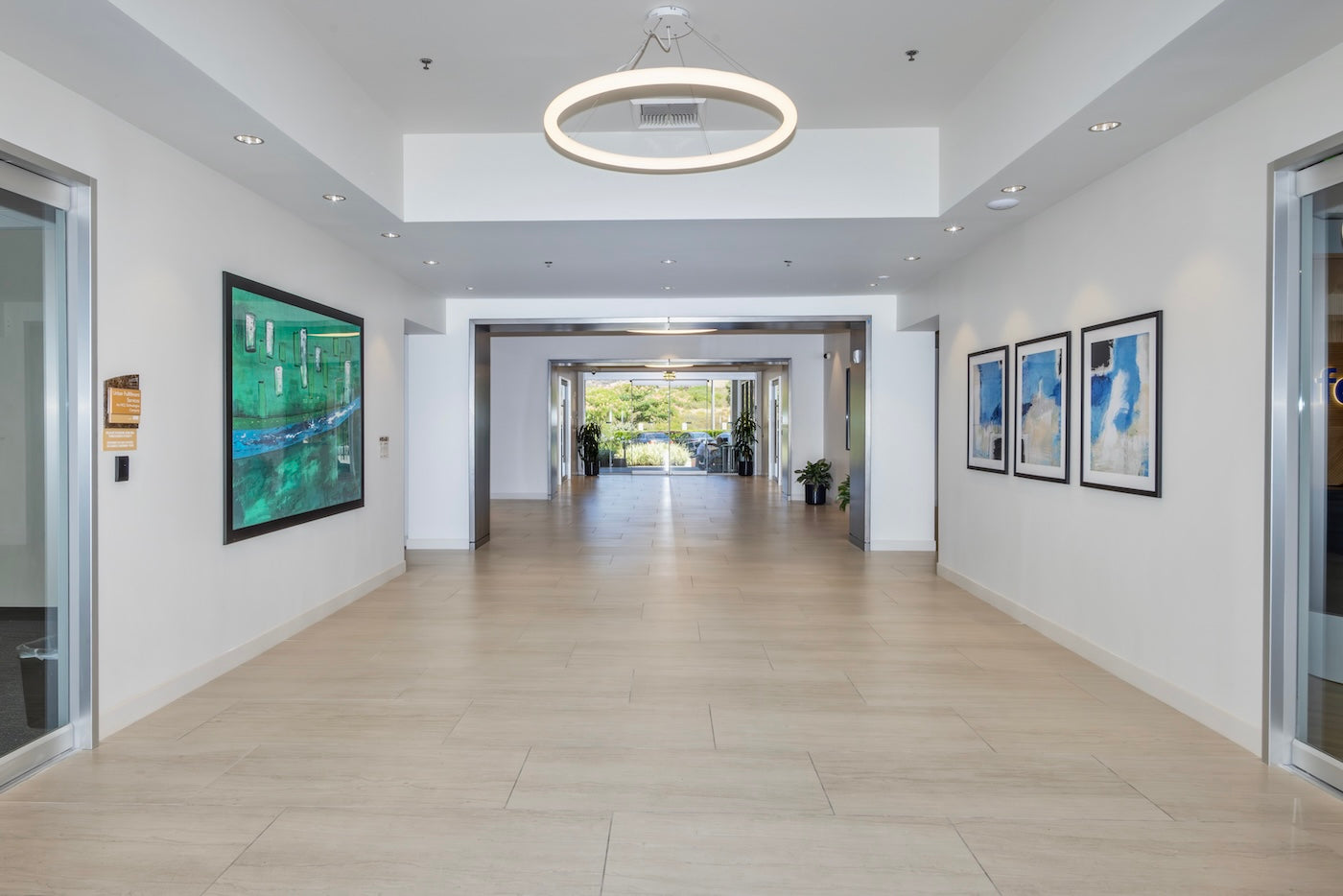 A bright, open corridor at Westlake Landmark features print reproductions of River Walk by Barbara Barnett on the left and Weather Conditions I–III by Cheryl Kinderknecht on the right. Together, the works balance tranquil greens and cool blues to echo the natural landscape and biophilic design elements throughout the building.
