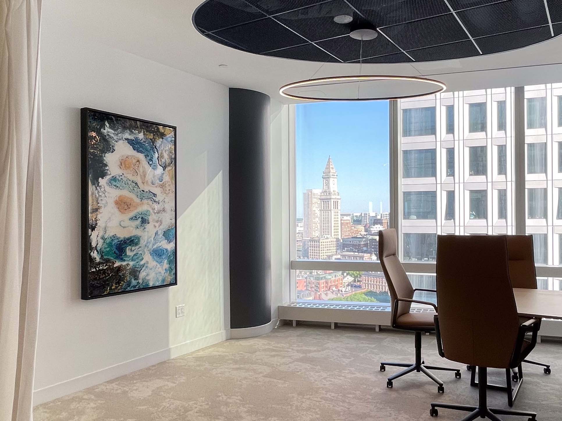Modern office space with large windows, chairs, and an original artwork on the wall.