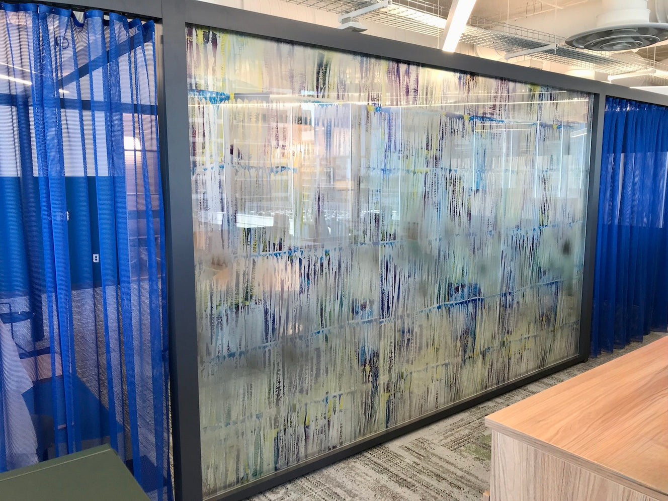 3. Glass partition framed in dark gray with Moving Through Emotions by Sierra Barnes. The glass decal features the artwork’s vertical streaks of blues, whites, purples, and yellows. The frosted-like pattern provides full privacy while adding depth and movement to the space.