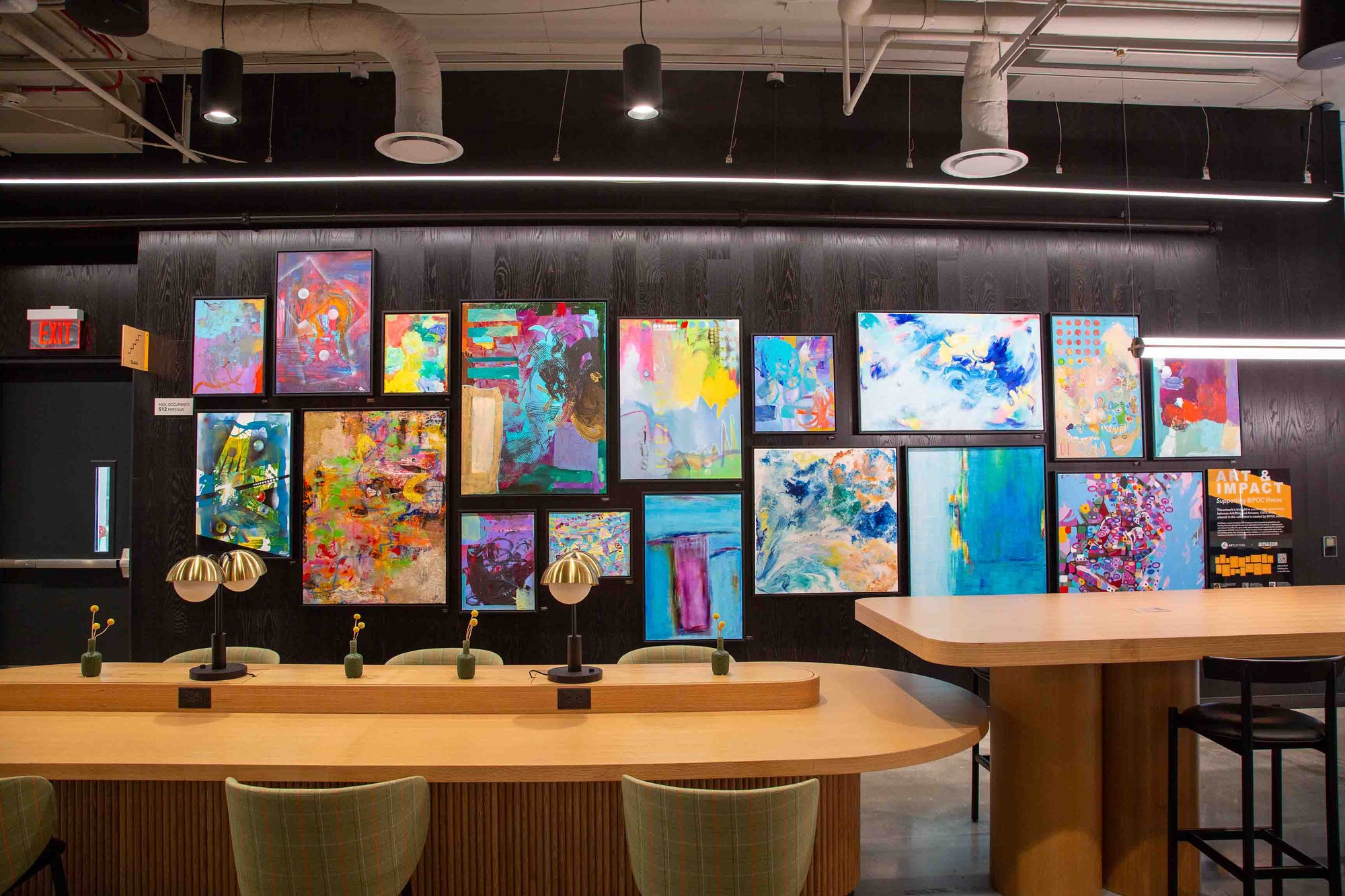 Art gallery with colorful abstract paintings on a wall above a co-working area.