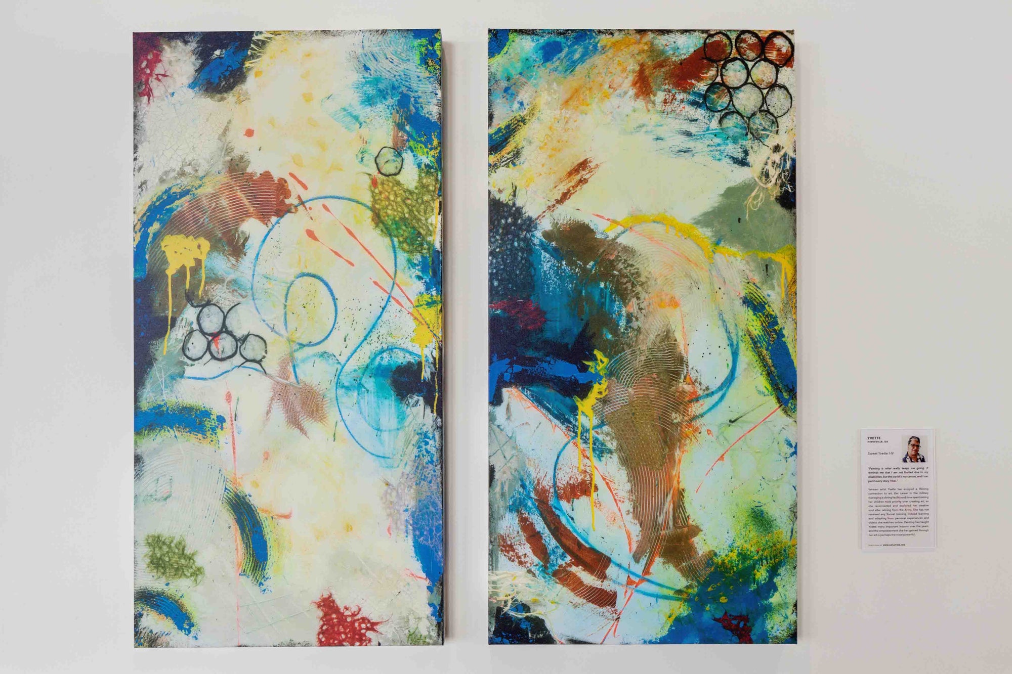 Two abstract paintings side by side on a white wall with a small label.