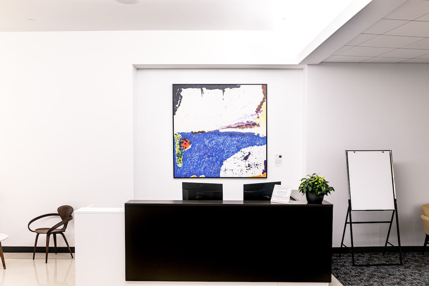Hanging above a reception desk, Abstract 2021-0519-15 by Han Huisman presents bold swaths of blue, black, white, and earthy tones with textured drips and organic marks.