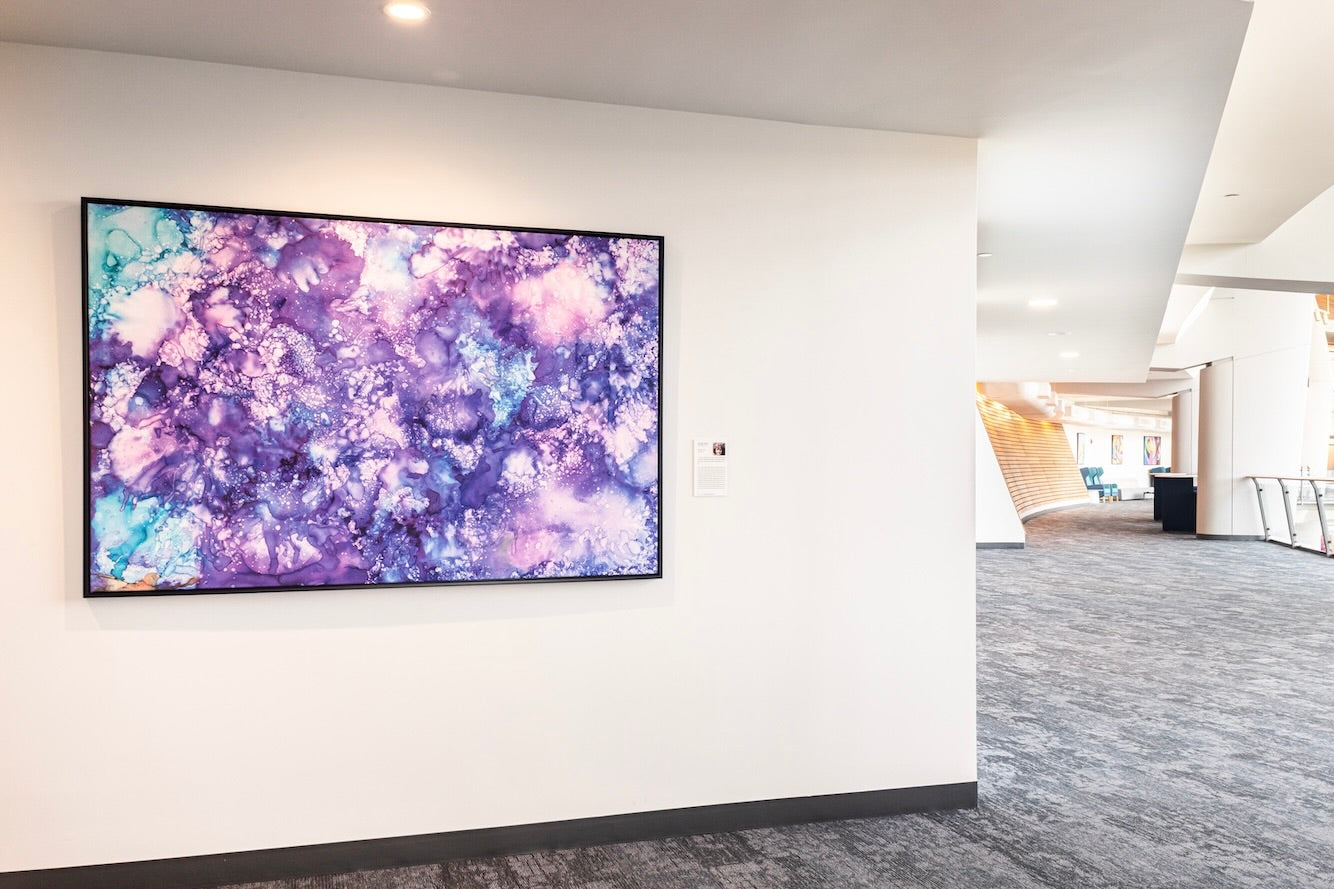 Reaching for the Stars by Selah Rose is a large abstract painting in shades of purple, pink, and blue with cloud-like textures, displayed on a white wall near an open hallway.