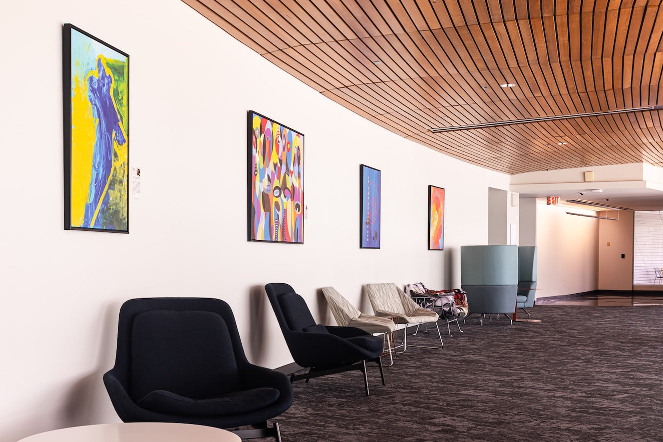 A series of prints by Yasmine Iskander, Kennedy Nganga, and Lisa Murphy hangs above a row of lounge chairs. 