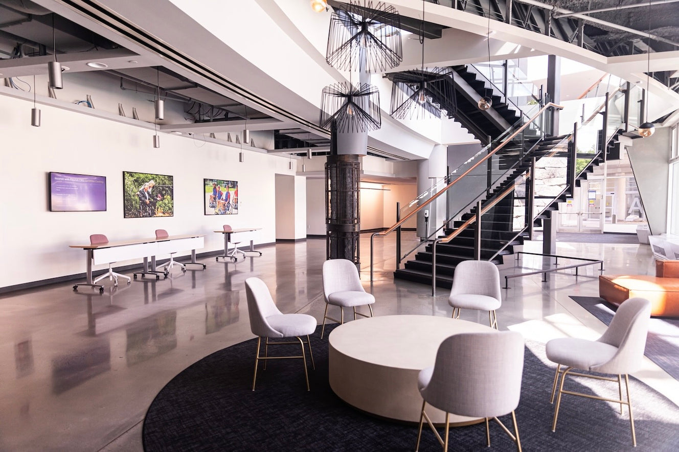 Two prints by Michaels Lyric are mounted on a wall near a modern staircase, both capturing people in dynamic outdoor scenes with expressive movement and bright, layered colors. 