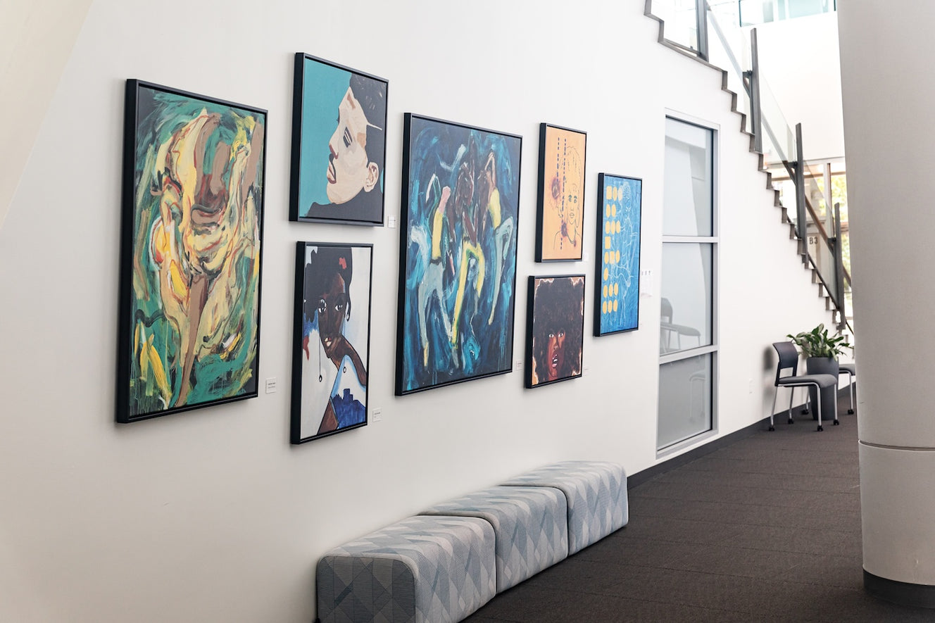 A gallery wall features prints by multiple ArtLifting artists, arranged salon-style above a cushioned bench. The collection includes portraits, abstract figures, and expressive color studies in a range of styles and tones.