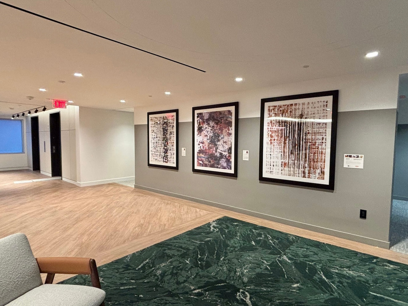 A seating area  at 777 6th St. NW. features two prints by ArtLifting artist Kari Souders and one by Diana de Avila, whose abstract compositions bring movement and depth to the modern setting, complementing the room’s natural wood flooring, green marble accents, and soft seating.