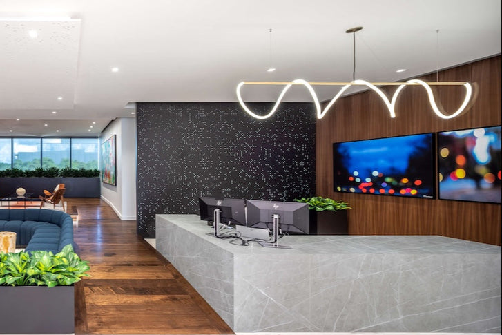 A wider view of the headquarters reception area, showing the front desk, seating area, and greenery. On the wall behind the desk are the same two framed prints of artworks by Damiano Austin, anchoring the space with bold color and abstract forms. 