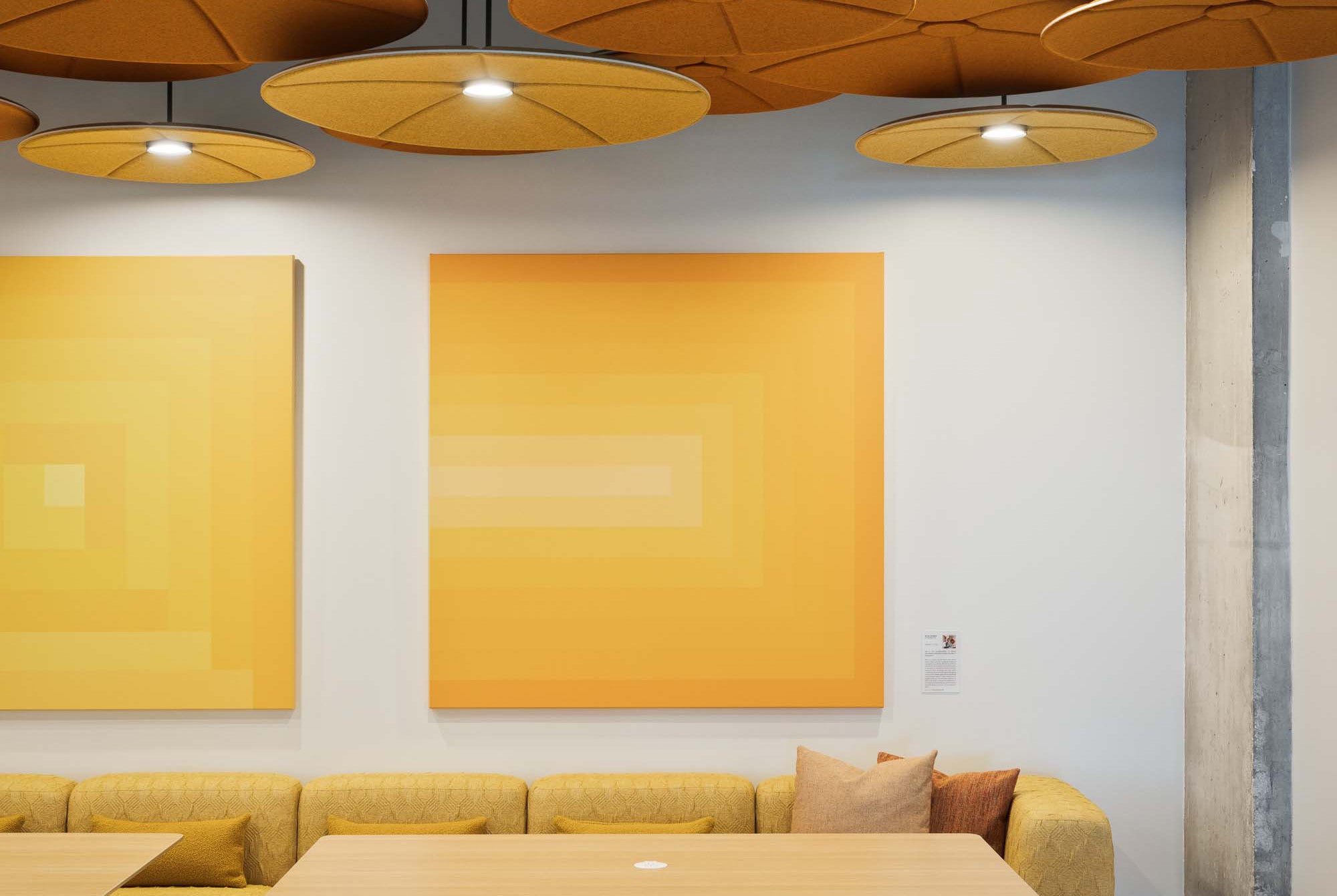 Modern interior with yellow abstract art on a white wall, a yellow sofa, and wooden tables.