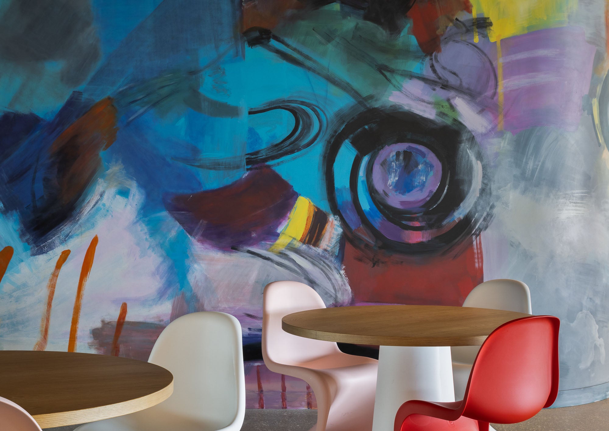 Modern interior with round tables and chairs in front of a colorful abstract wall mural.